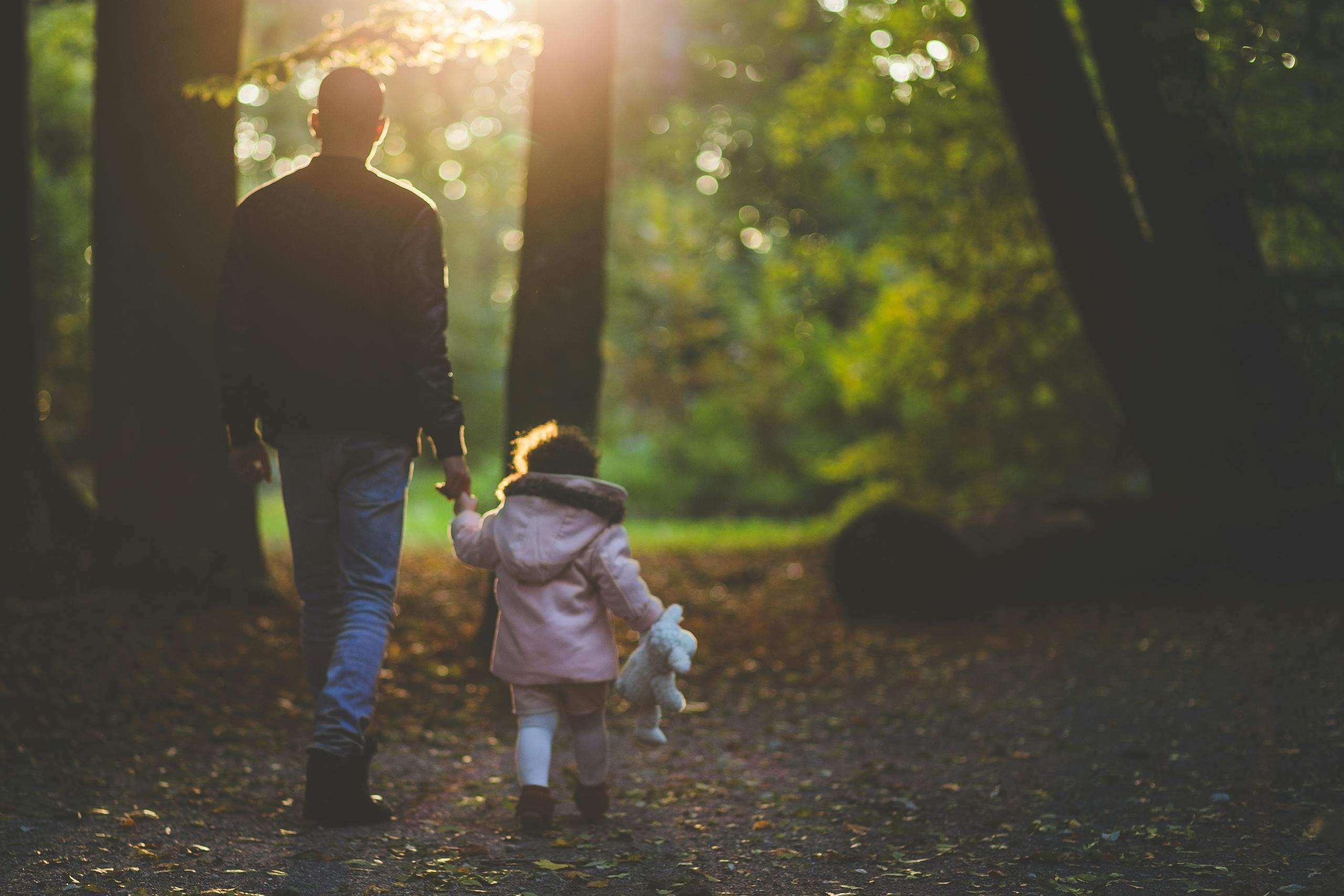 A father and daughter holding hands while walking in a park during autumn.