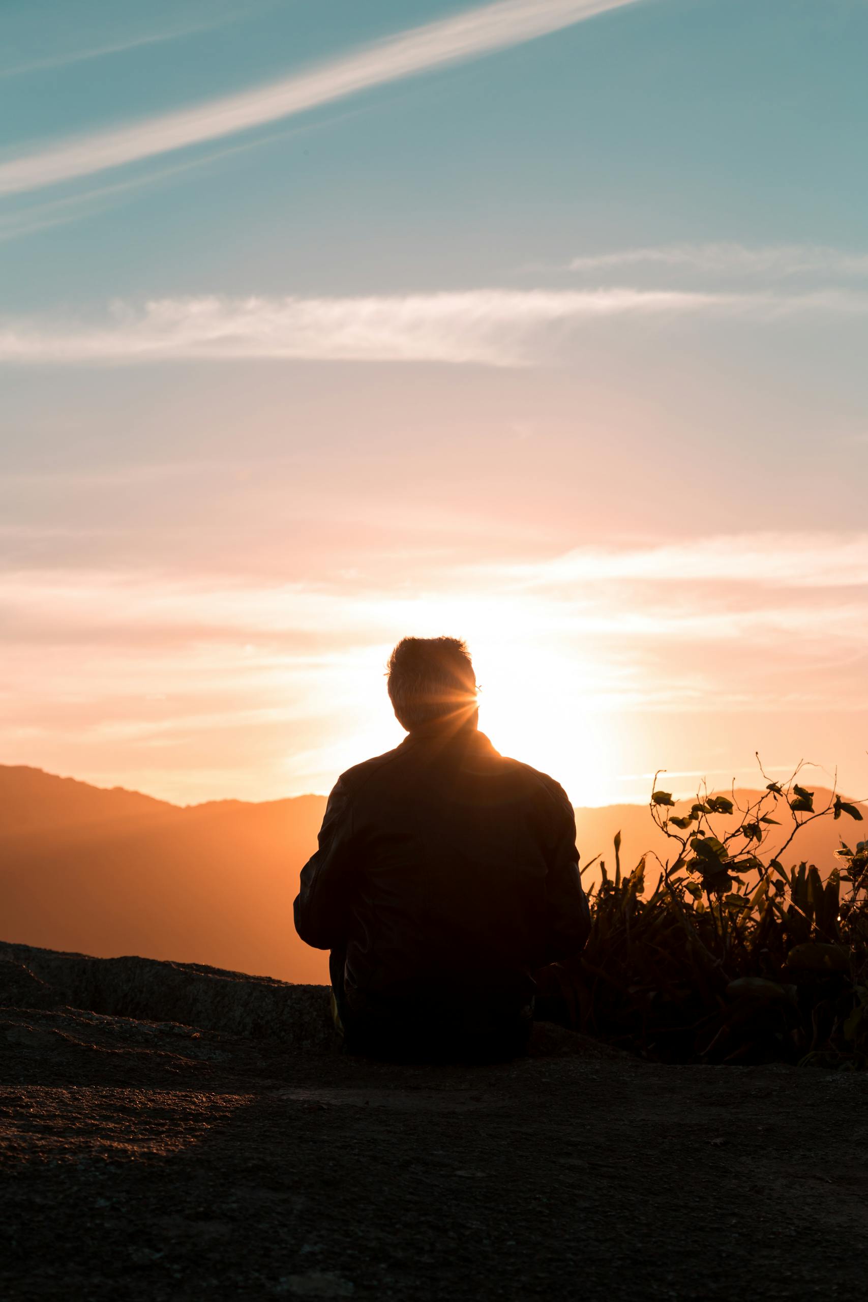 A lone person sitting and enjoying the scenic view of sunset on a hilltop.